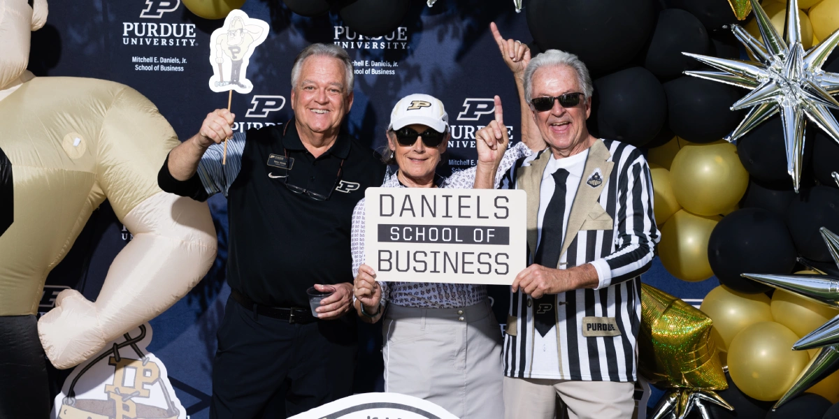 three alumni hold a sign for the Daniels School of Business at a tailgate party