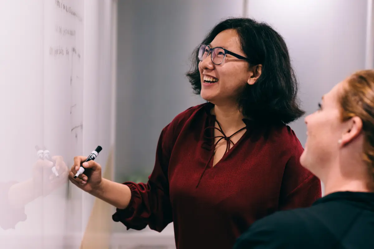 Graduate student solving equation on whiteboard