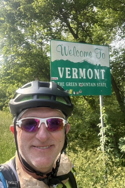 Hummels in a bike helmet before a sign that reads Welcome to Vermont