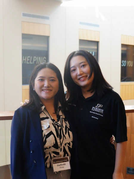 Sisters, one seeking master’s level human resources management training and the other seeking a master’s education in marketing, standing together inside a Purdue University building.