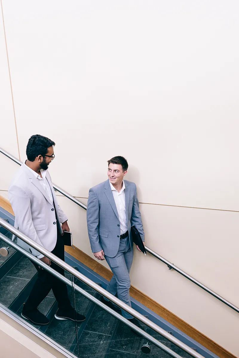 Two people in suits walking down stairs having a discussion.