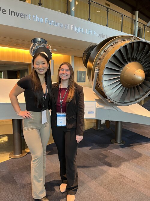 Two students stand in front of an aircraft engine