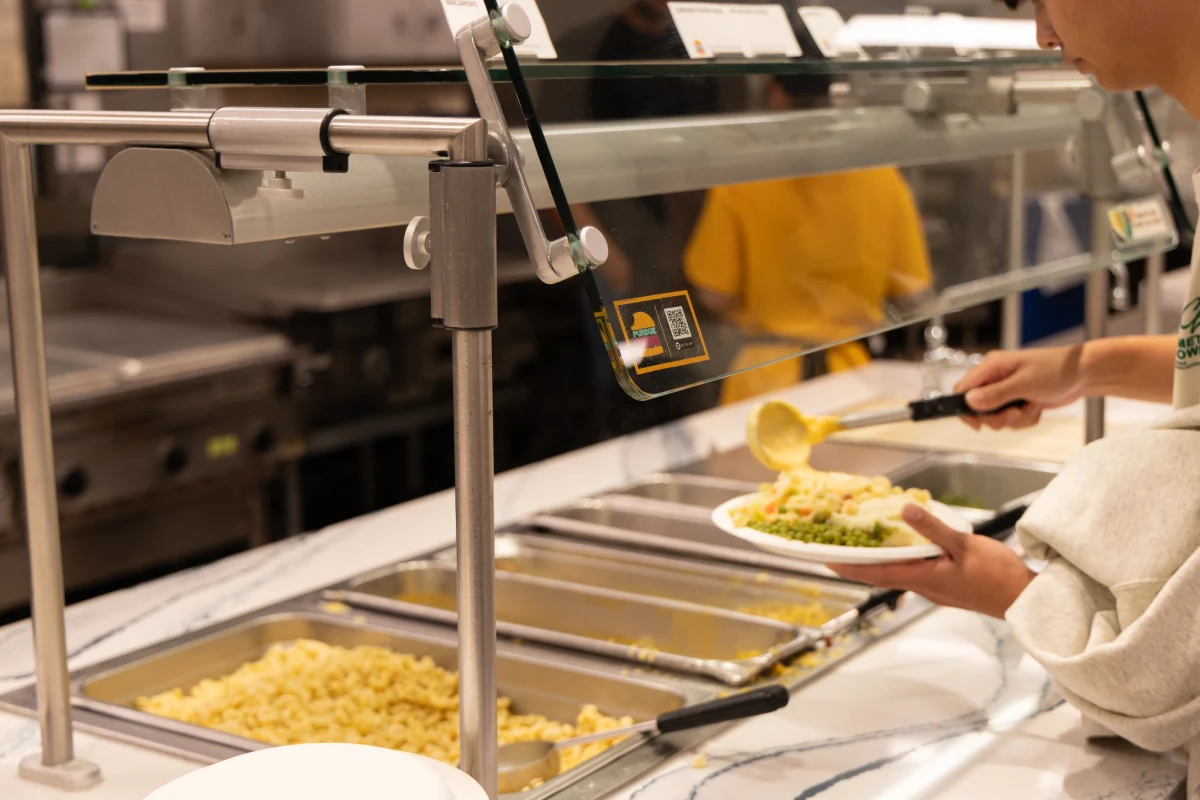 student putting a plate of food together from hot bar